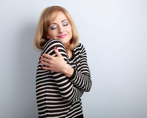 Happy makeup blond woman hugging herself with natural emotion on enjoying face with close eyes. Love concept by yourself